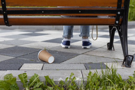 a paper cup is lying under a bench on which a person is sitting. high quality photo