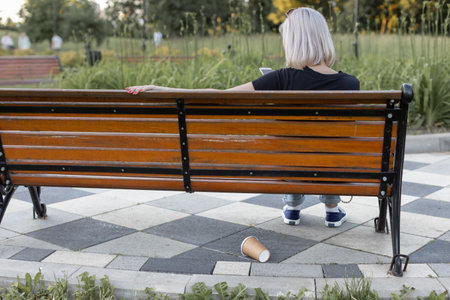 a paper cup is lying under a bench on which a person is sitting. high quality photo