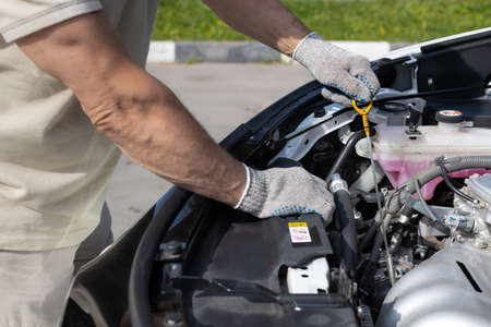 a man checks the oil level in a car engine. a man stands near the raised hood of the car and checks...