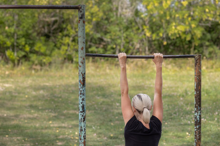 girl hanging on the crossbar on the sports ground. Woman hanging on a bar
