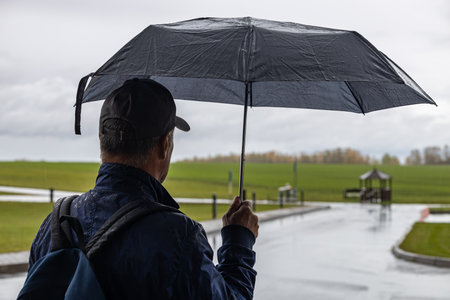 Moscow, Russia - October 01, 2022: a man stands under an umbrella in rainy weather. man holding an umbrellaのeditorial素材