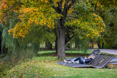 Moscow, Russia - October 01, 2022: woman lying in the park with a phone. woman lying on a sun loungerのeditorial素材