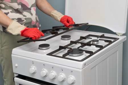 man in gloves washes gas stove at home. woman cleaning gas burner. high quality photoの写真素材