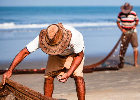 Morjim, North GOA, India , 29 March 2016: fisherman in a hat clean the fishing net on the ocean. man in a hat. the fisherman takes out the catch.のeditorial素材