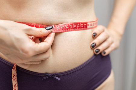 woman measuring her waist with a measuring tape, shot with shallow depth of field. woman holding a measuring tape. pregnant woman measuring belly size.の写真素材