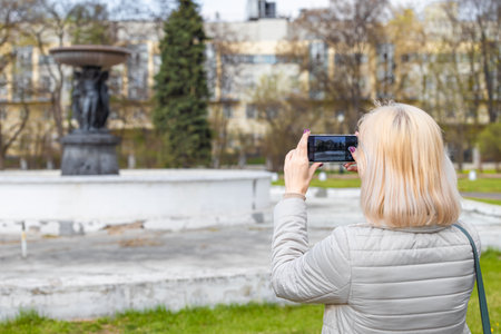 Moscow, Russia - April 22, 2023: Tourist shoots an old fountain on a smartphone. woman photographing old architectureのeditorial素材