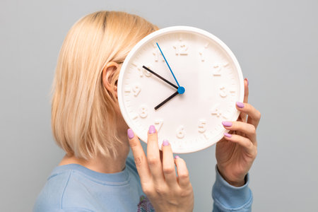 a woman holds a large round white watch in her hands. time does not wait. person's age. clock...