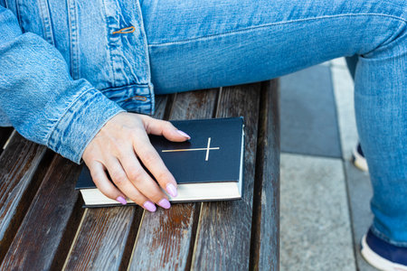 woman holding her hand on the bible lying on the bench. woman holding paper bible. high quality...