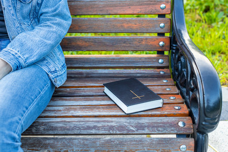 the bible lies on the bench next to the woman. a closed bible lies on a bench next to a woman. high...