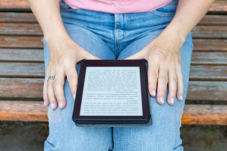 woman reading an e-book sitting on a park bench. reading a book built on electronic ink technology. high quality photoの写真素材