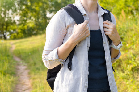a woman holding a backpack on her back by the straps. a girl with a backpack walks along a path in...