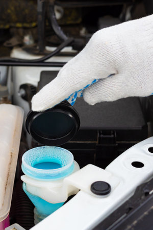 the driver pours fluid into the washer reservoir. washer fluid. glass cleaner. man closes the lid of the windshield wiper barrel.の写真素材