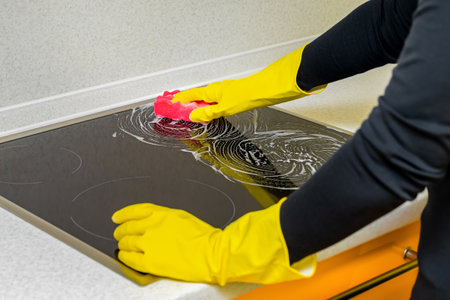 woman in rubber gloves washes the hob in the kitchen. washing the hob in the kitchen.の写真素材