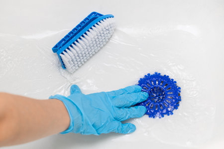 woman in gloves cleans bathtub with brush. drain hole in the bathtub. bath careの写真素材
