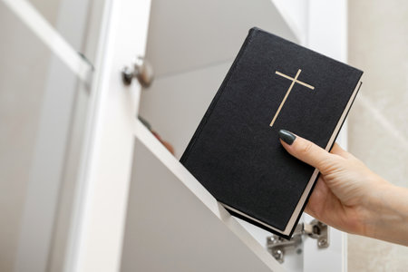 woman takes out a bible from a bookcase. hand removes bible from bookshelf