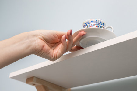 a woman's hand removes coffee utensils from the kitchen shelf. man takes an empty coffee cup. coffee utensils. dishes on the kitchen shelf. cup with ornament. High quality photoの写真素材