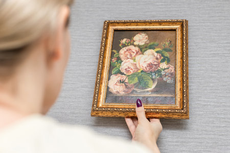 woman a picture of flowers on the wall hanging. man hanging a picture on the wall. picture on the...