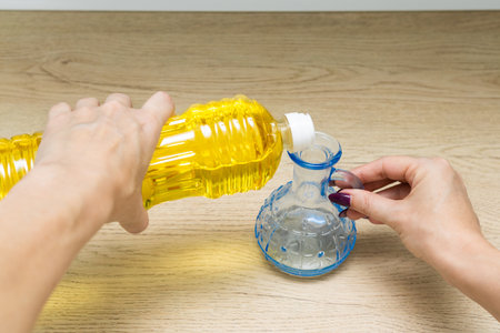 housewife pours sunflower oil into a glass bottle. man pours oil from a plastic bottle into a glass...