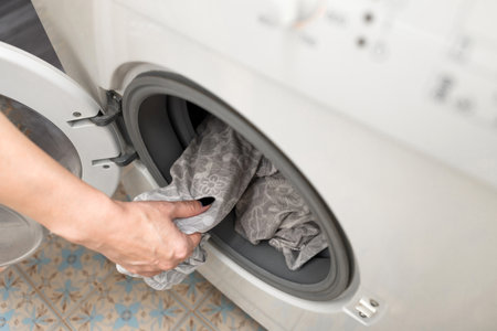housewife takes out washed clothes from the drum of the washing machine. washing bed linen in a...