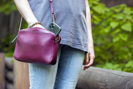 woman takes out a smartphone from a handbag, close-up. woman in the park takes out a smartphone from...