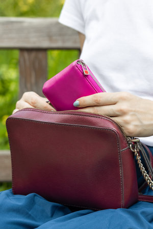 woman takes out a wallet from a lady's handbag. woman's hand takes out a wallet from a bag. woman in...