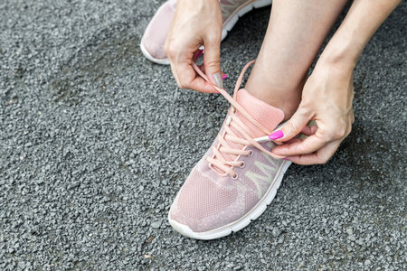 woman laces up sneakers while jogging in the park. the hand inserts the lace into the eyelets. man...