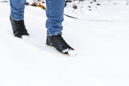 man in black leather boots walking on white snow. a man walks on untouched snow. snow on the toes of...