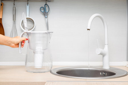 housewife pouring water into water filter in kitchen. woman filling water filter in kitchen sink. jug shaped water filter.の写真素材