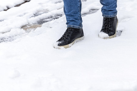 man in black leather boots walking on white snow. snow on the toes of boots. snowy path in the city. first snowの写真素材