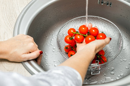 woman washing cherry tomatoes in kitchen sink. housewife washes tomatoes before cooking. woman washes tomatoes bought in the store. tomatoes on a branch. High quality photoの写真素材