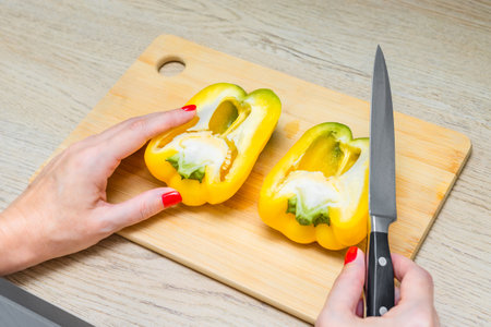 woman cutting yellow bell pepper with knife on kitchen board. cut bell pepper lies on a kitchen wooden board. chef cutting yellow bell pepper.の写真素材