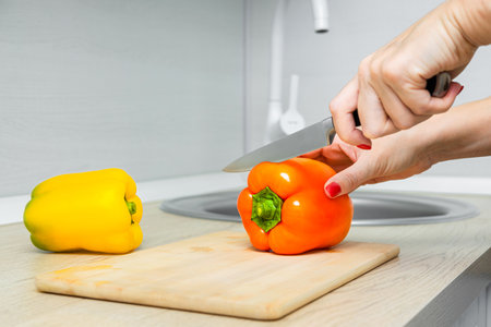 woman cutting bell pepper with knife on kitchen board. chef cutting red bell pepper. knife cuts bell pepperの写真素材