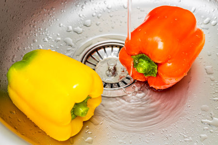 two bell peppers are lying in the kitchen sink. woman washing red bell peppers in kitchen sink. bell pepper in the kitchen.の写真素材