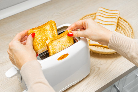 woman hand takes fried toast out of toaster, close-up. woman takes fried bread out of toaster....