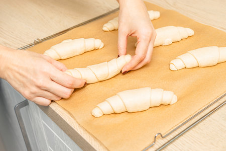 woman placing croissant on baking sheet, close-up. baking tray with croissants. housewife making croissants in home kitchen, close-up. woman baking croissants. uncooked croissant. unbaked croissantの写真素材
