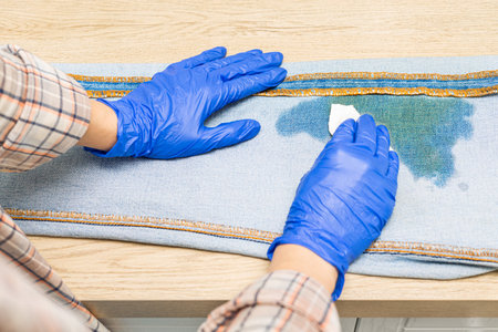 woman removing dirty stain on jeans, close-up. dirty stain on jeans. man removes grease stain from...
