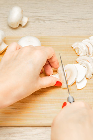 woman cutting mushrooms on wooden board in kitchen, first person view. housewife cuts champignon mushrooms. Vertical photoの写真素材