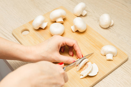 woman cutting mushrooms on wooden board in kitchen. housewife cuts champignon mushrooms. cooking mushrooms at home.の写真素材