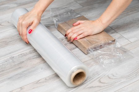 man wrapping cardboard box with transparent stretch film. woman packing a parcel. sending an online...