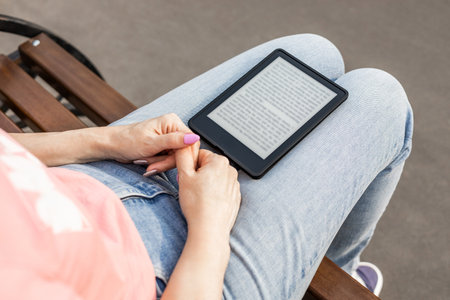 woman reading e-book sitting on bench, close-up. man reading an e-book. an e-book lies on a girl's lap. ebook mockupの写真素材