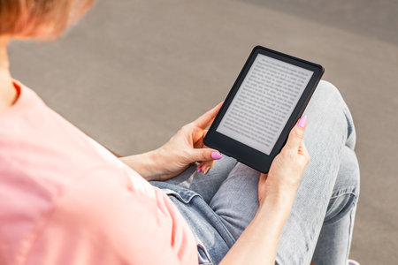 woman reading e-book sitting on bench, close-up. man reading an e-book.の写真素材