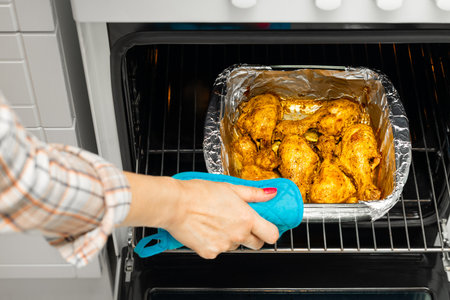 housewife takes fried chicken legs out of the oven. cooking chicken legs at home. cooking chicken legs in the oven. chicken in foilの写真素材