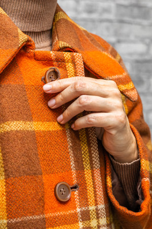 a woman fastening the top button of her coat, vertical photo. A woman unbuttons her coat. women's fingers fastening a button. woman putting on coat. woman trying on coat. autumn coat top button.の写真素材