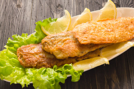 Fried fish with lemon and lettuce on a wooden table, horizontal