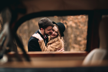 Gorgeous newlywed bride and groom posing in pine forest near retro car in their wedding day.の写真素材