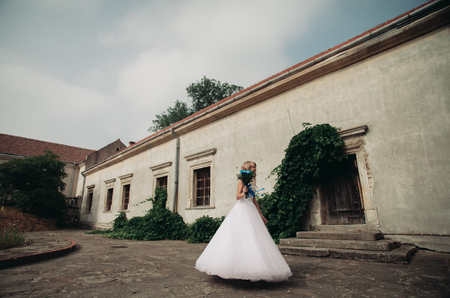 Beautiful young blond bride with bridal bouquet sitting on the stairs under gorgeous plants.の写真素材