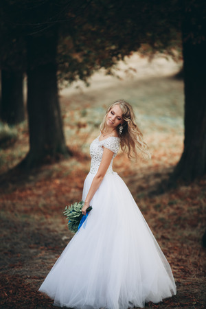Beautiful young blond bride with bridal bouquet sitting on the stairs under gorgeous plants.の写真素材