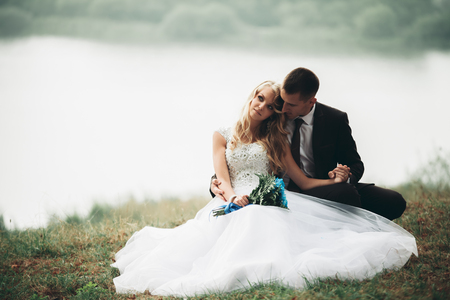 Happy wedding couple sitting on the ground near the lake.の写真素材