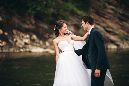 Beautifull wedding couple kissing and embracing near the shore of a mountain river with stones.の写真素材