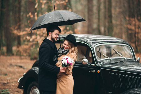 Romantic fairytale wedding couple, bride and groom, kissing and embracing in pine forest near retro car.の写真素材